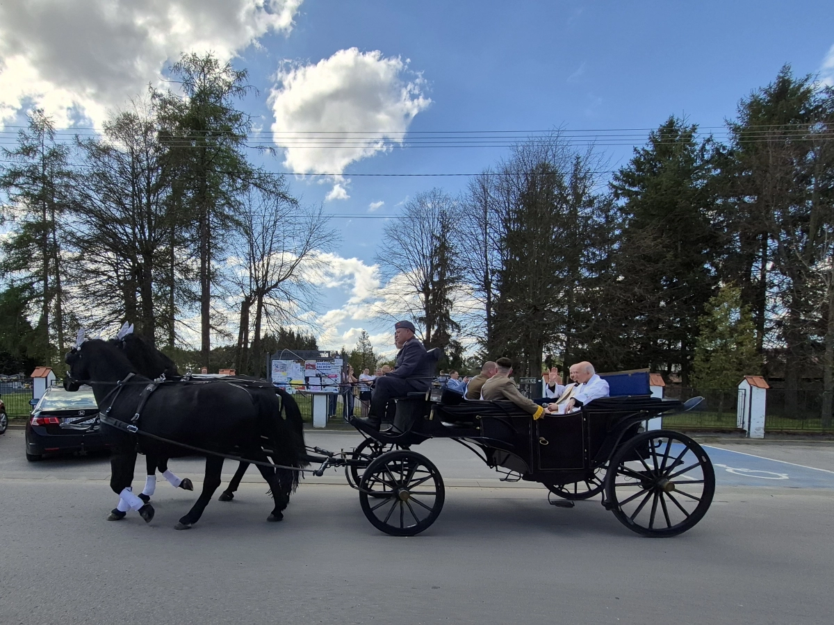 Zaprzęg konny z bryczką na ulicy, w środku księża i mężczyźni w mundurach..