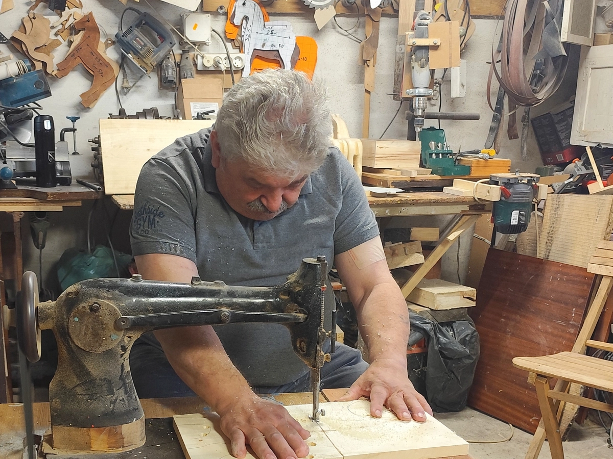 Mężczyzna siedzący przy maszynie w pracowni przy obróbce deski drewnianej.