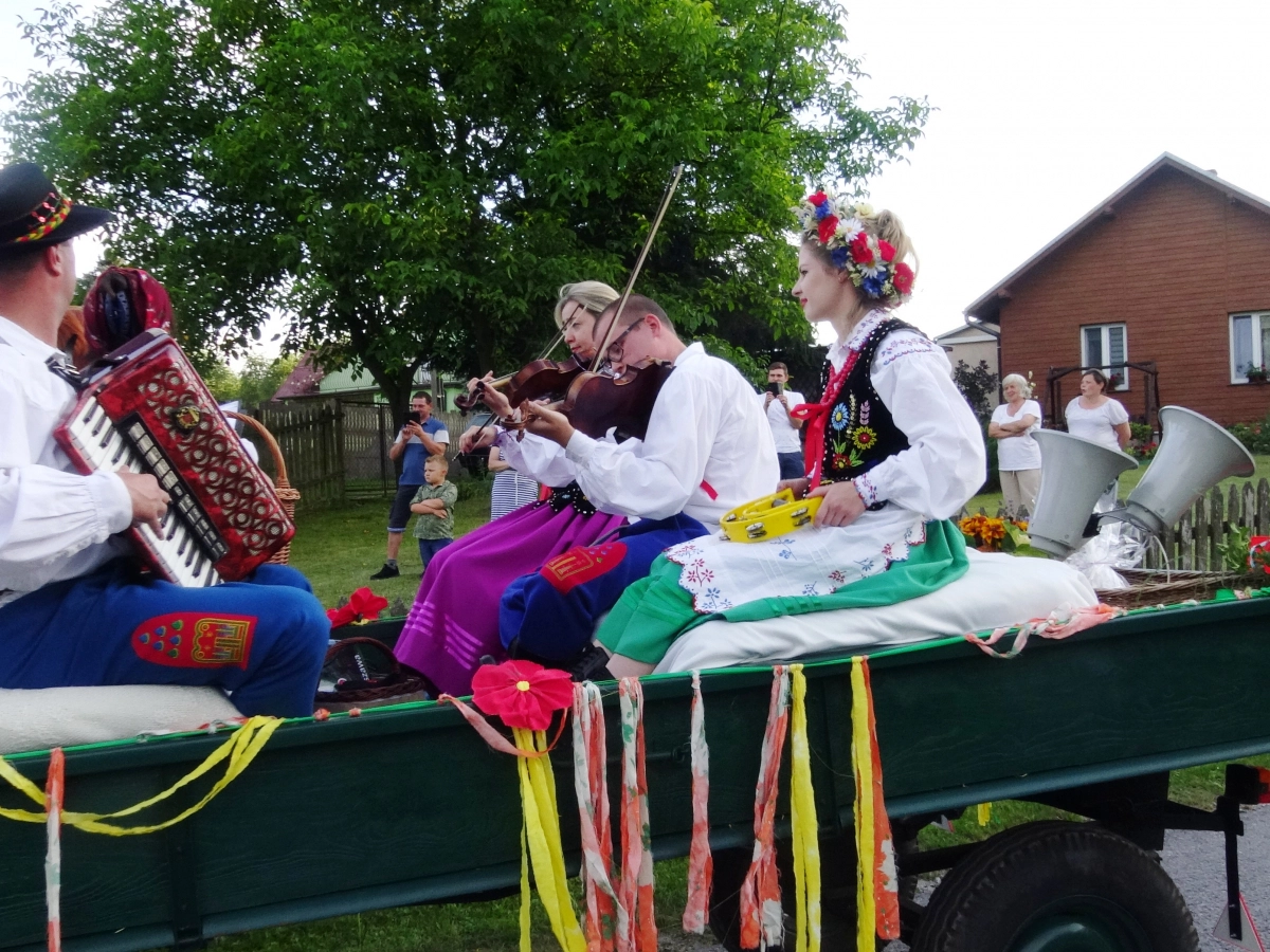 Kapela ludowa w tradycyjnych strojach gra na wozie jadącym ulicą, udekorowanym wstążkami.