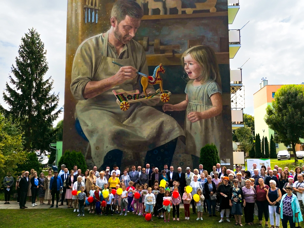 Zdjęcie grupowe. Uczestnicy uroczystości pozują przy muralu.
