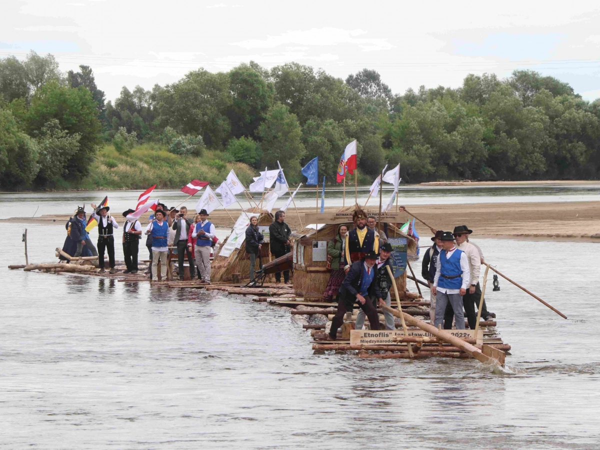 Flisacy w tradycyjnych strojach płyną tratwą po rzece podczas współczesnego spławu.