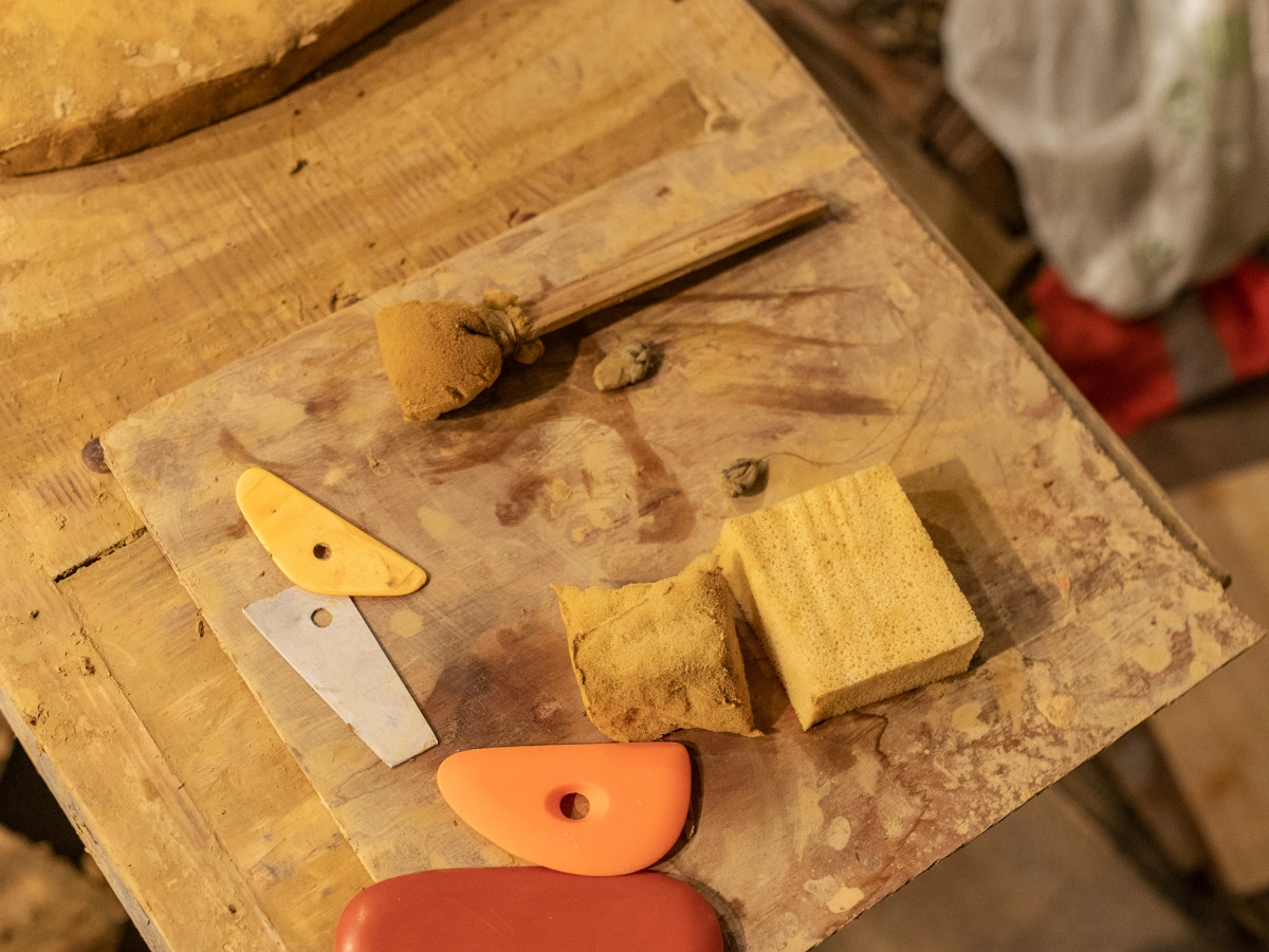 Na drewnianym stole leżą narzędzia i gąbki używane do pracy z gliną.