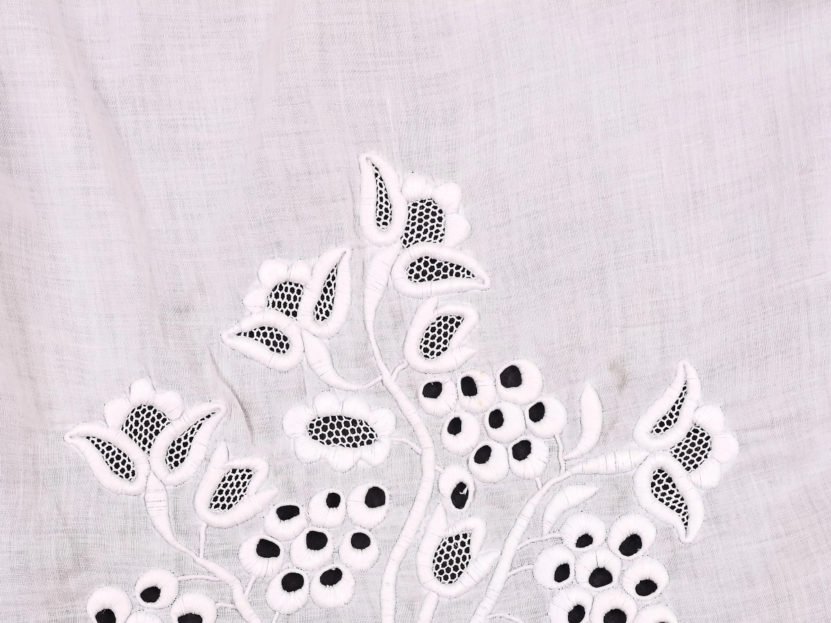 Biała tkanina z elementami haftu z motywem roślinnym.