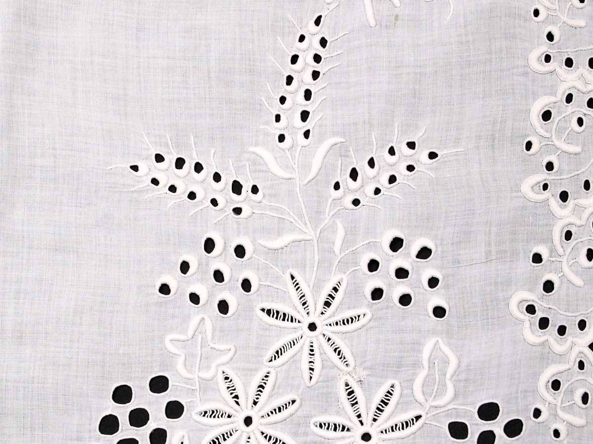 Biła tkanina z elementami haftu z motywem kwiatów i zboża.