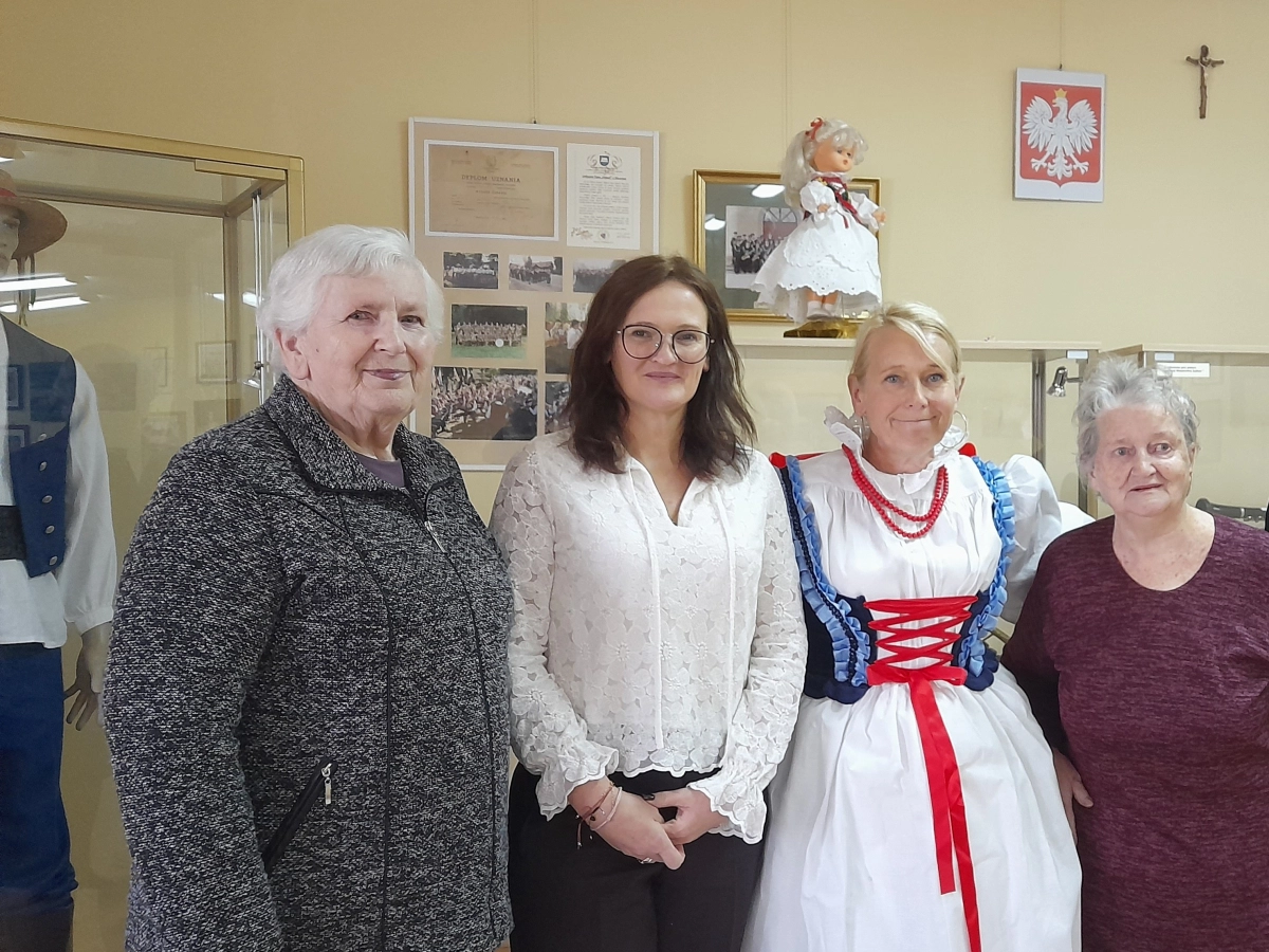Cztery kobiety pozują do zdjęcia w muzeum, jedna z nich w tradycyjnym ludowym stroju.