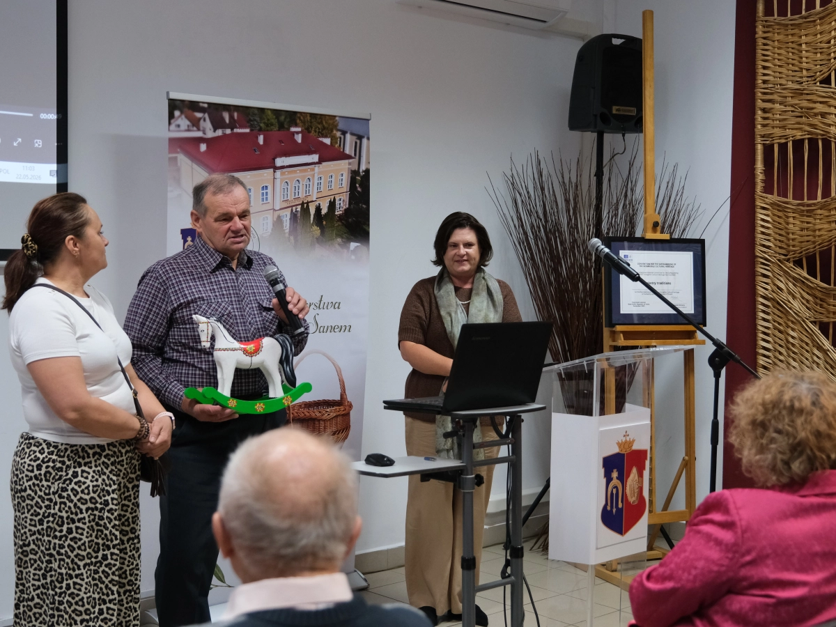 Mężczyzna przemawia do uczestników konferencji, trzymając w rękach kolorowego konika na biegunach.