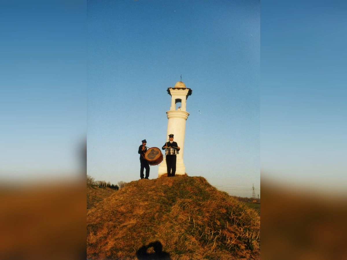 Dwóch mężczyzn w mundurach stoi na wzgórzu i gra na bębnach obok białej wieży.