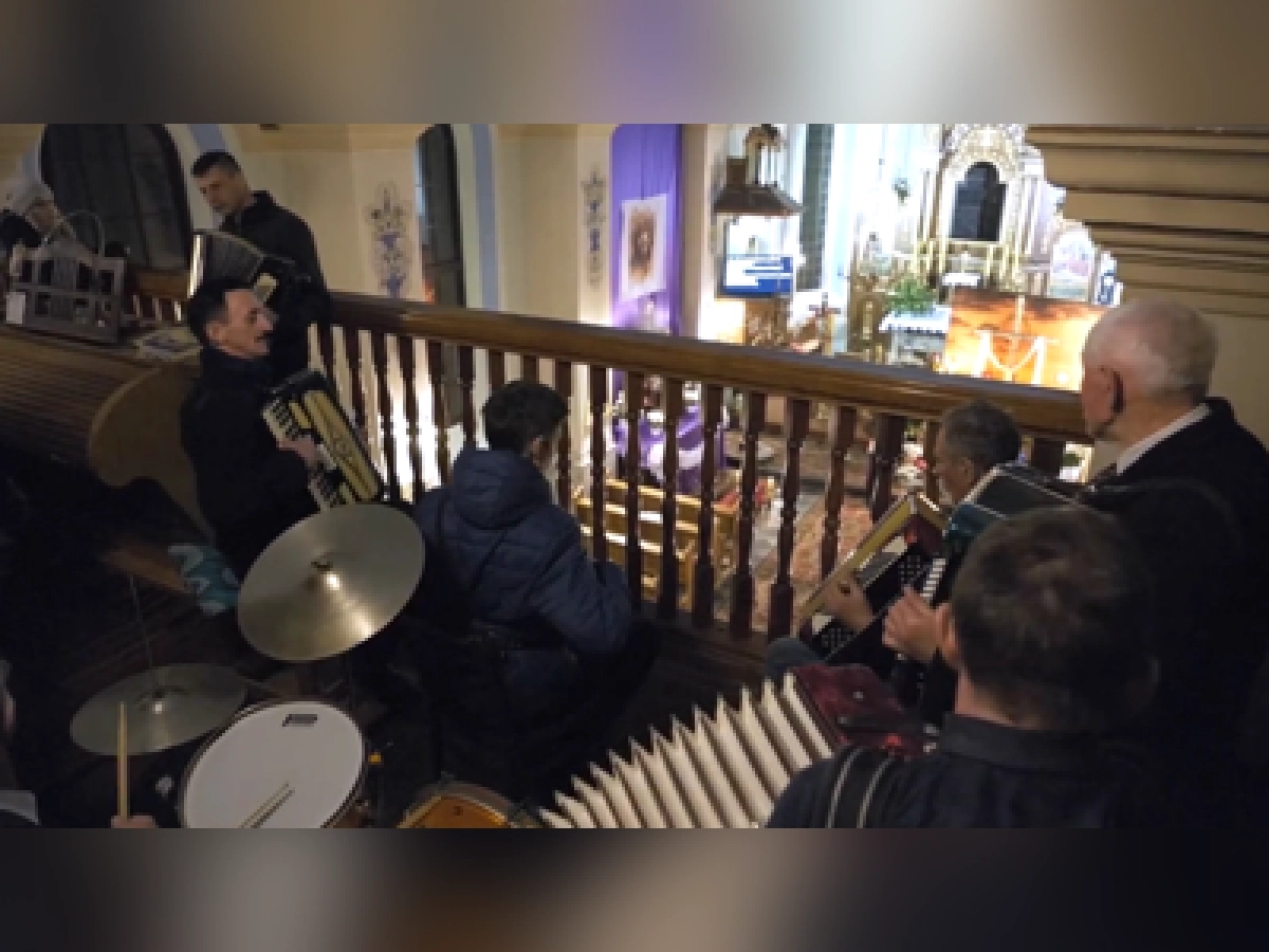Muzycy grają na instrumentach na chórze kościoła, w tle widoczne wnętrze świątyni i ołtarz.