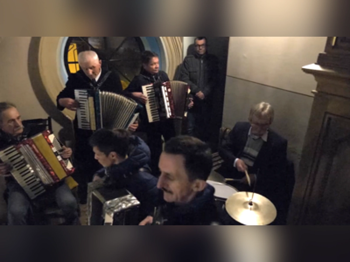 Grupa muzyków gra na akordeonach i perkusji we wnętrzu budynku.