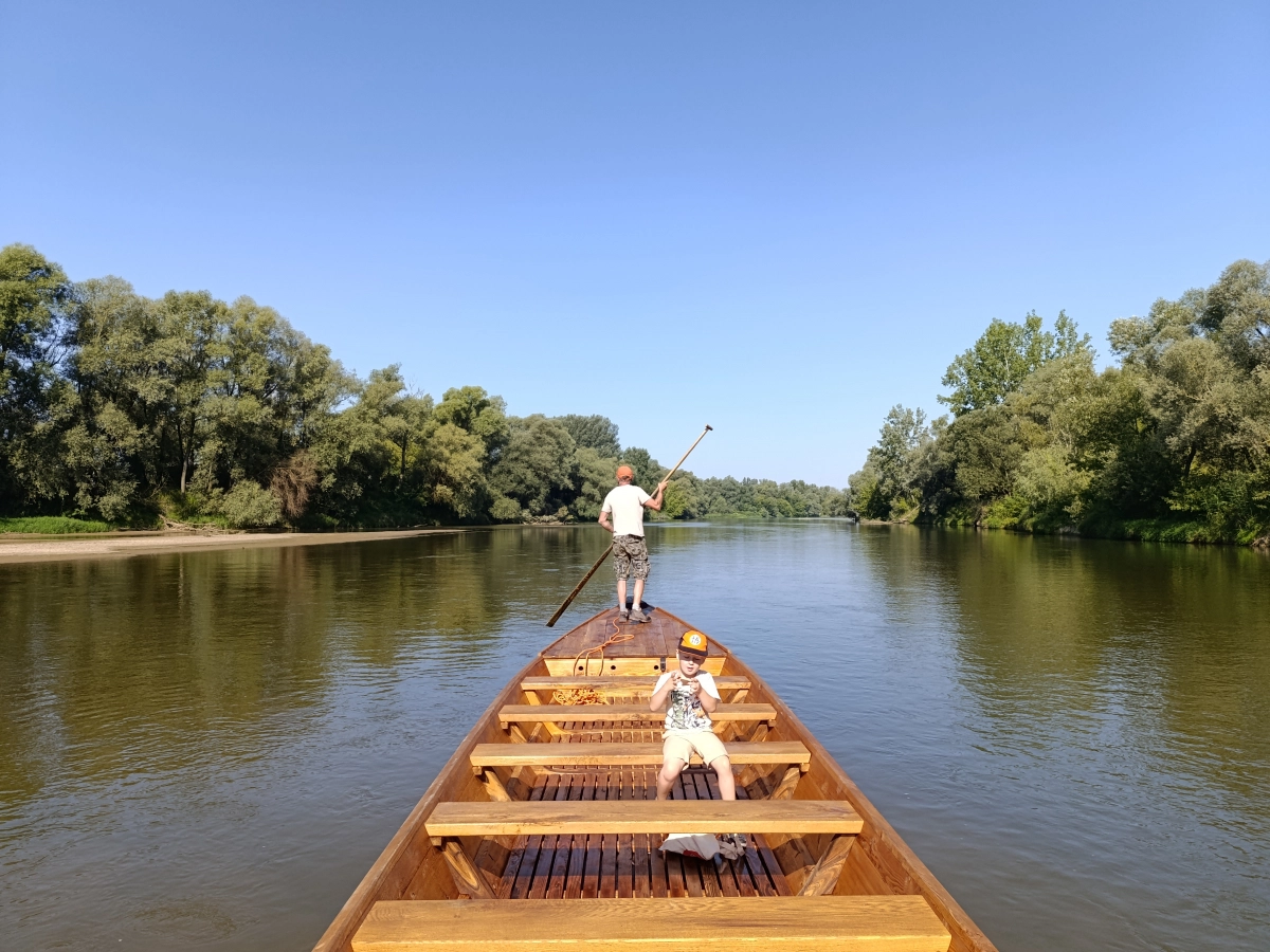 Długa drewniana łódź sterowana przez mężczyznę płynie przez rzekę.